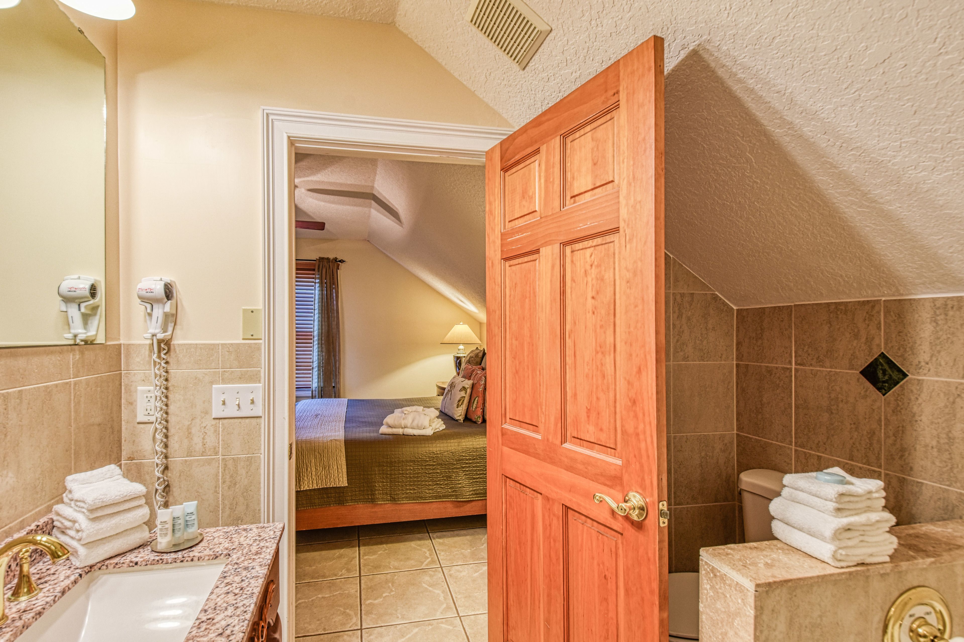 A bathroom with a sink, towel stack, and a wooden door leading to a bedroom.