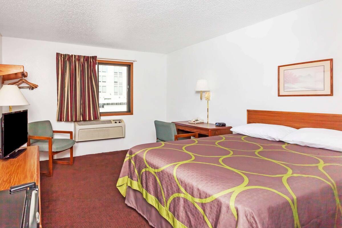 Una habitación de hotel con cama, escritorio, silla, televisión y aire acondicionado.