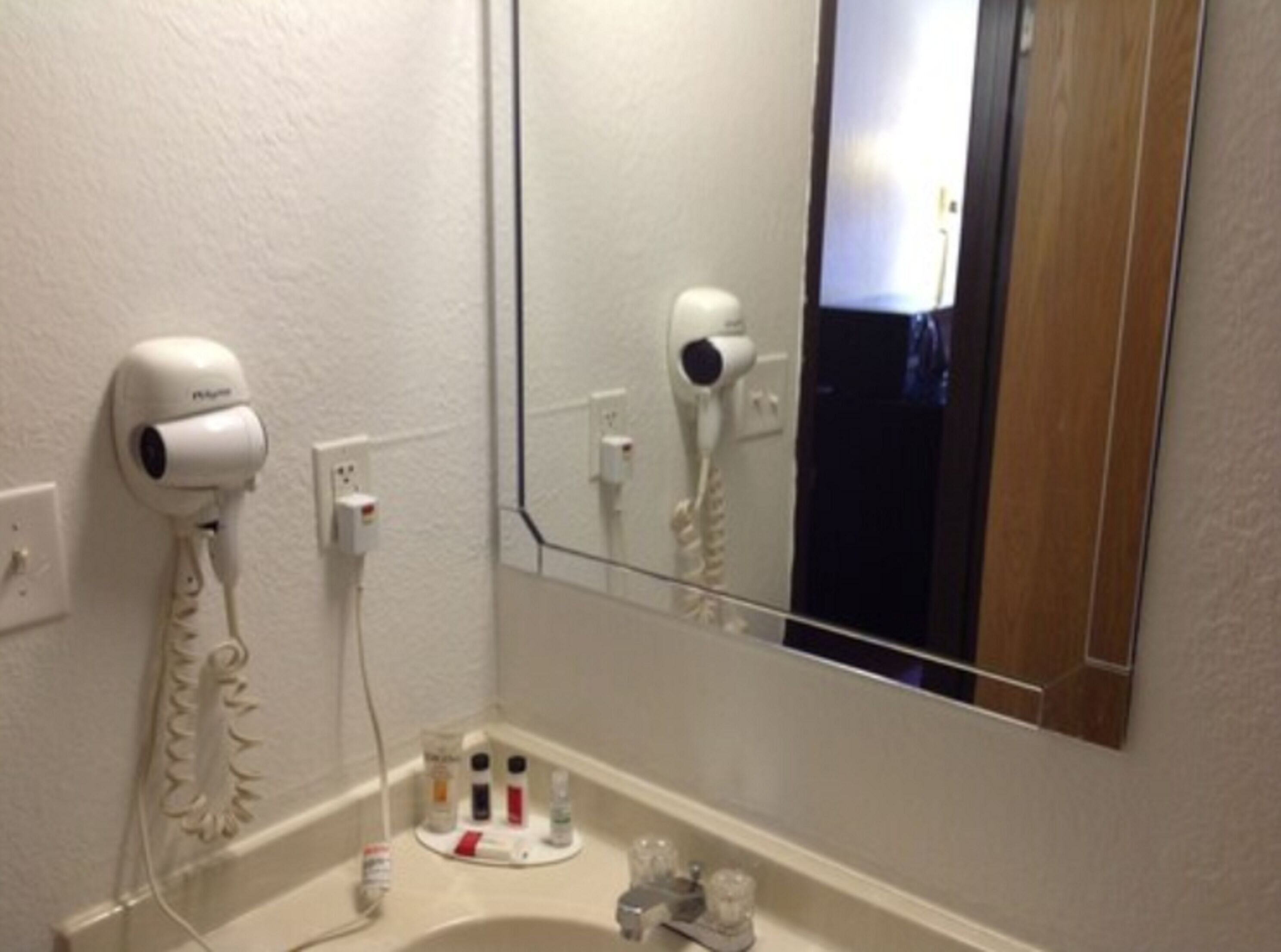 Un baño con un lavamanos blanco, un espejo y dos secadores de pelo fijados en la pared.