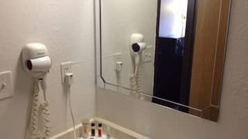 Un baño con un lavamanos blanco, un espejo y dos secadores de pelo fijados en la pared.