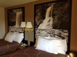 Une chambre d’hôtel avec deux lits, une table de chevet, une lampe et deux tableaux représentant des cascades, accrochés au mur.