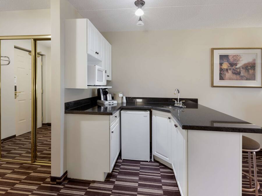 A compact kitchen with white cabinets, a black countertop, a microwave, and a small refrigerator.