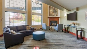 A spacious lobby with a fireplace, comfortable seating, and large windows offering a view of the outdoors.