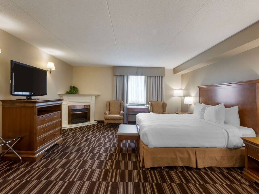 Ein Hotelzimmer mit einem großen Bett, einem Fernseher, einem Schreibtisch mit Stuhl, einem Kamin und einem Fenster mit Vorhängen.