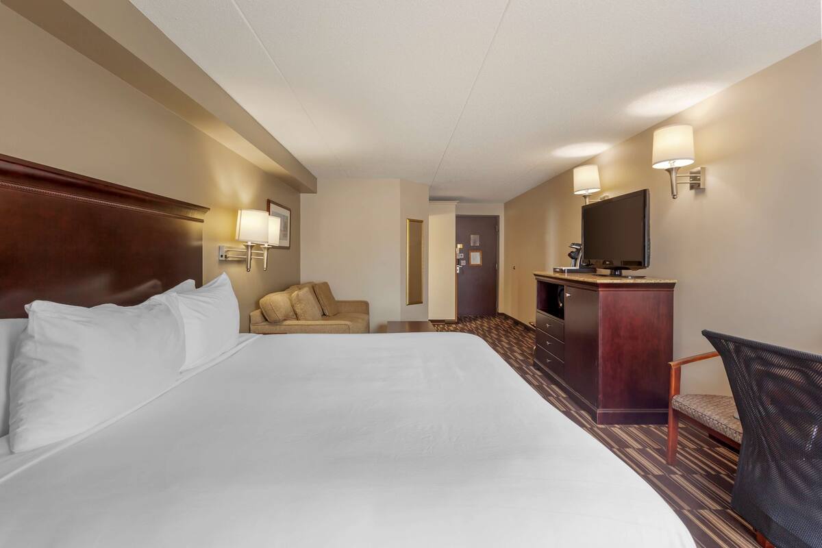 A hotel room with a large bed, a desk, a television, and a chair.