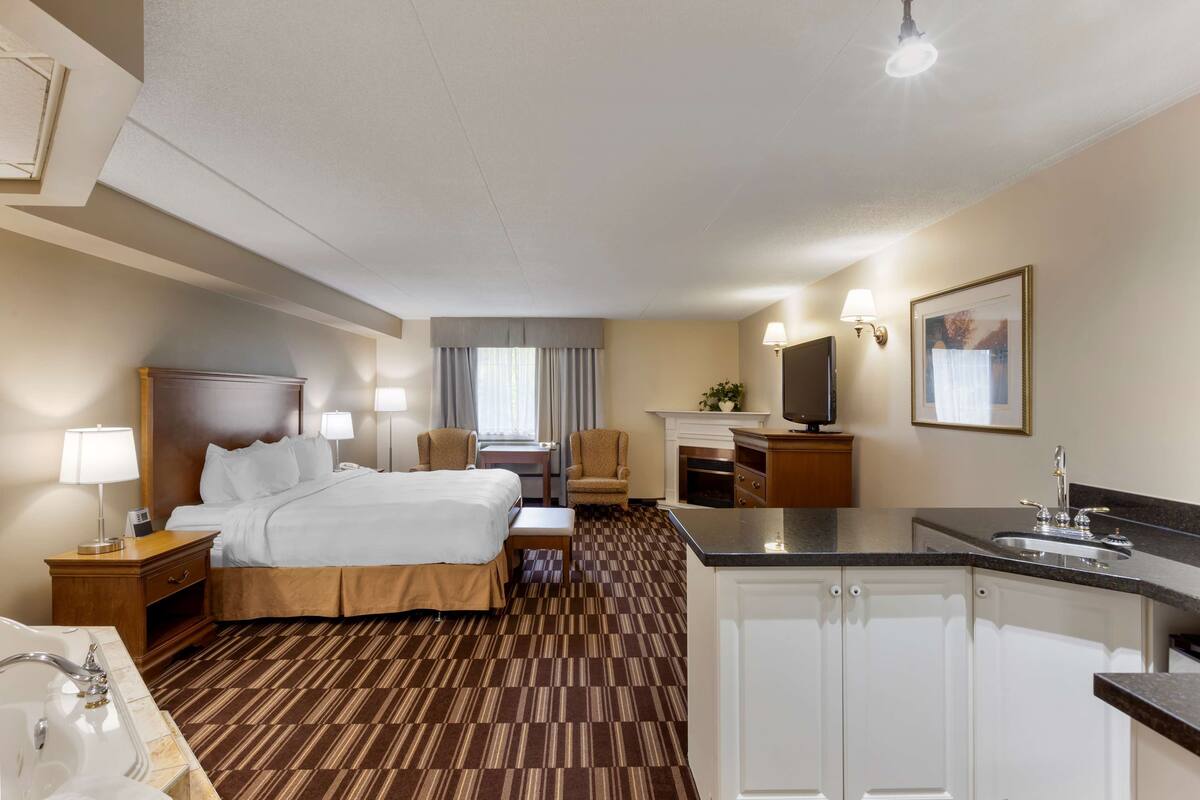 A hotel room with a large bed, a desk, a chair, a TV, a sink, and a cabinet.