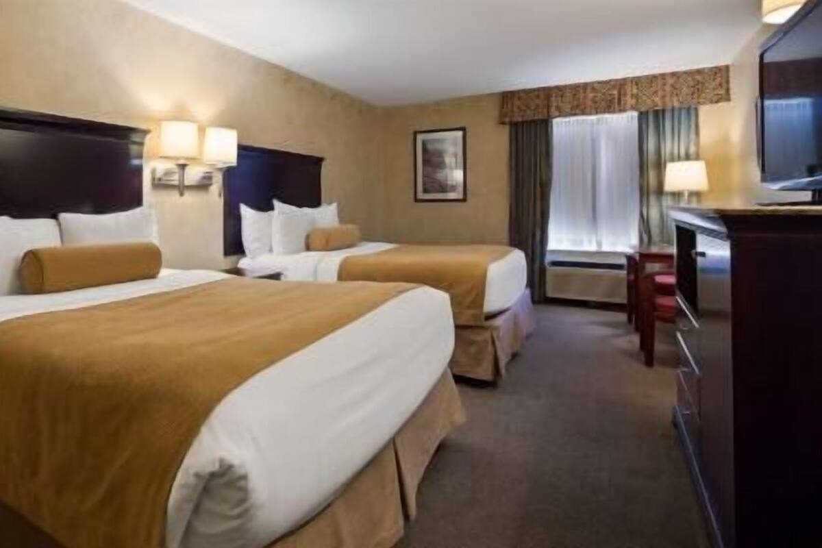 A hotel room with two beds, a desk, a chair, and a television.