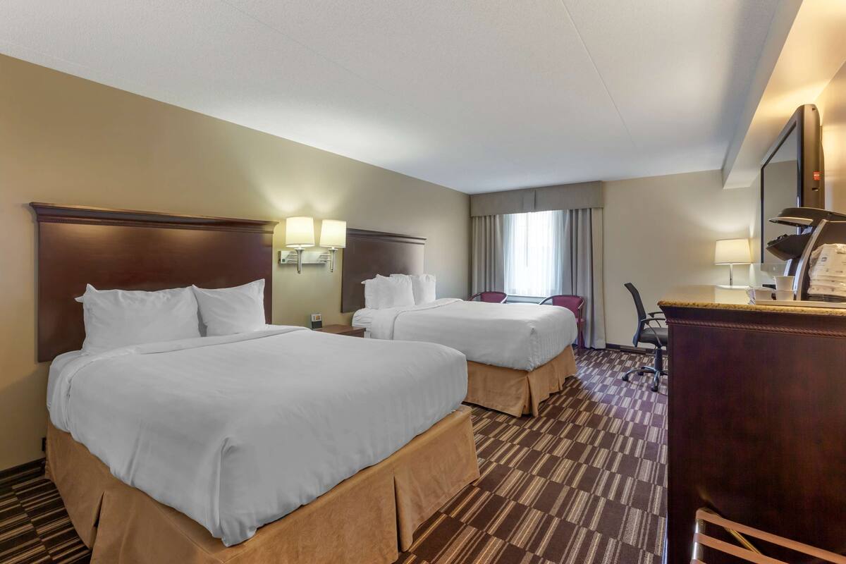 A hotel room with two beds, a desk, a chair, and a large mirror.