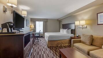 A hotel room with a bed, a desk with a computer, a TV, a sofa, and a lamp.