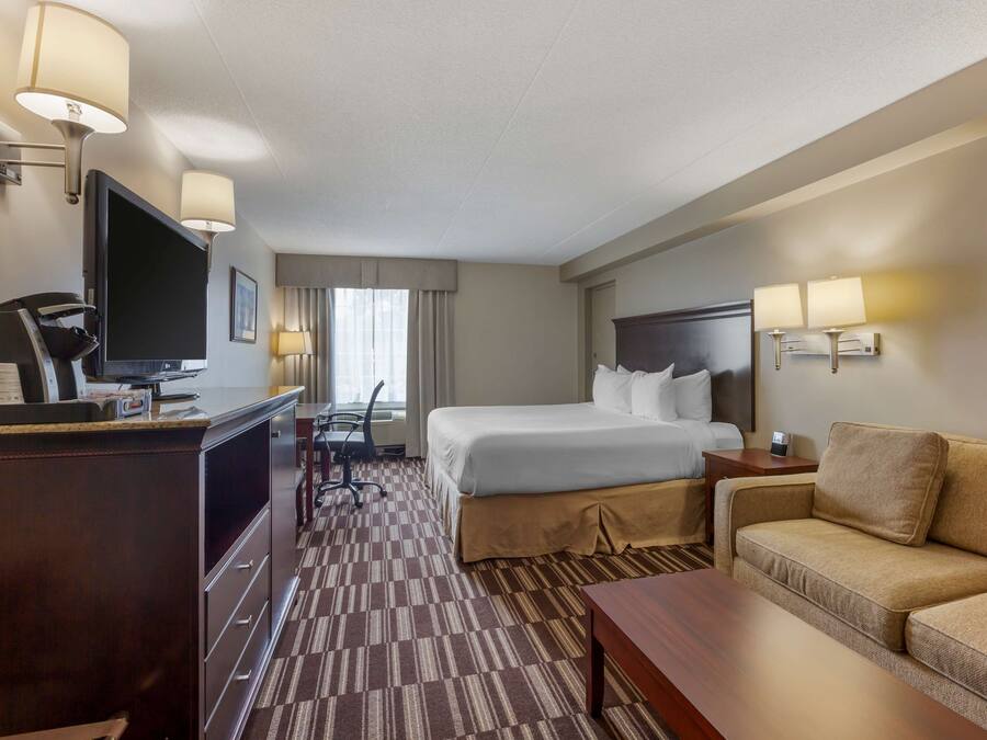 A hotel room with a bed, a desk with a computer, a TV, a sofa, and a lamp.