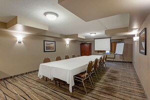 Una sala de conferencias con una larga mesa, sillas, una pantalla de proyector y una pizarra.