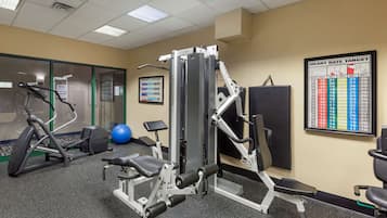 A gym with various exercise equipment, including a treadmill, weight machines, and a wall chart displaying heart rate targets.