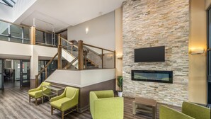 Un hall d’entrée spacieux doté d’un plancher en bois, de sièges recouverts d’un tissu vert, d’un escalier et d’un téléviseur à écran plat fixé à un mur texturé.