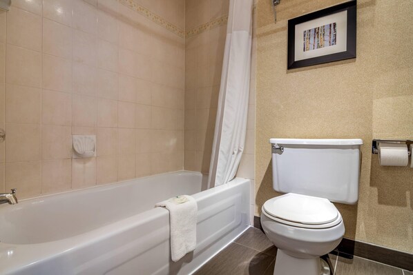 A bathroom with a bathtub, toilet, and a framed picture on the wall.