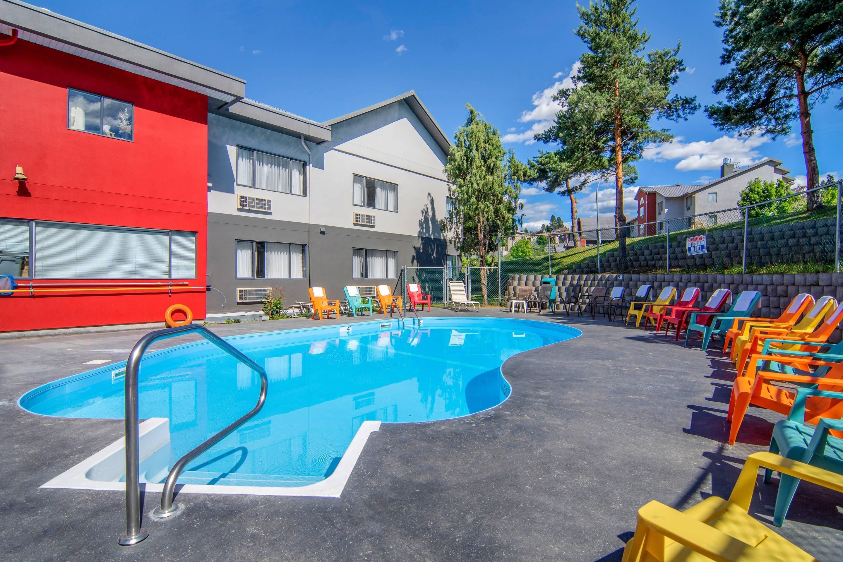 A swimming pool with a metal ladder, surrounded by colorful lounge chairs and a building with multiple windows.