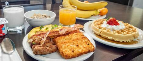 A breakfast plate with waffles, scrambled eggs, bacon, sausages, and toast.