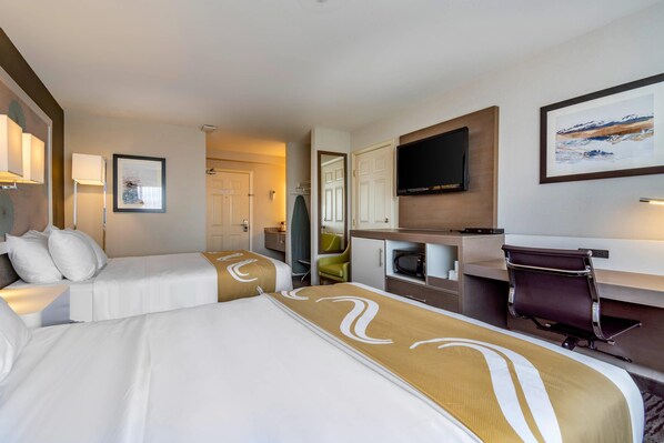 A hotel room with two beds, a desk, a chair, a television, and artwork on the walls.