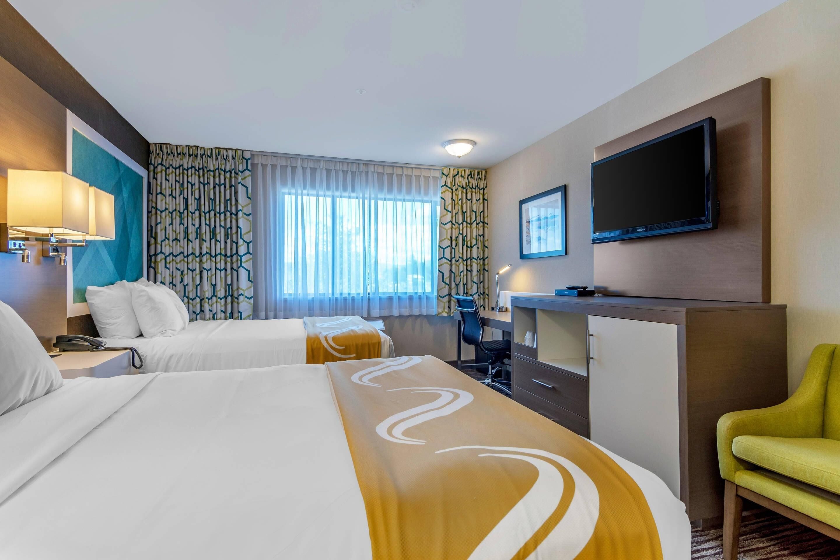 A hotel room with two beds, a desk, a TV, and a green chair.