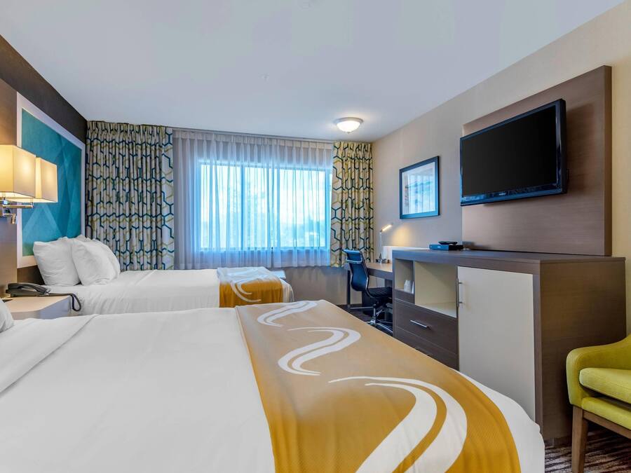 A hotel room with two beds, a desk, a TV, and a green chair.