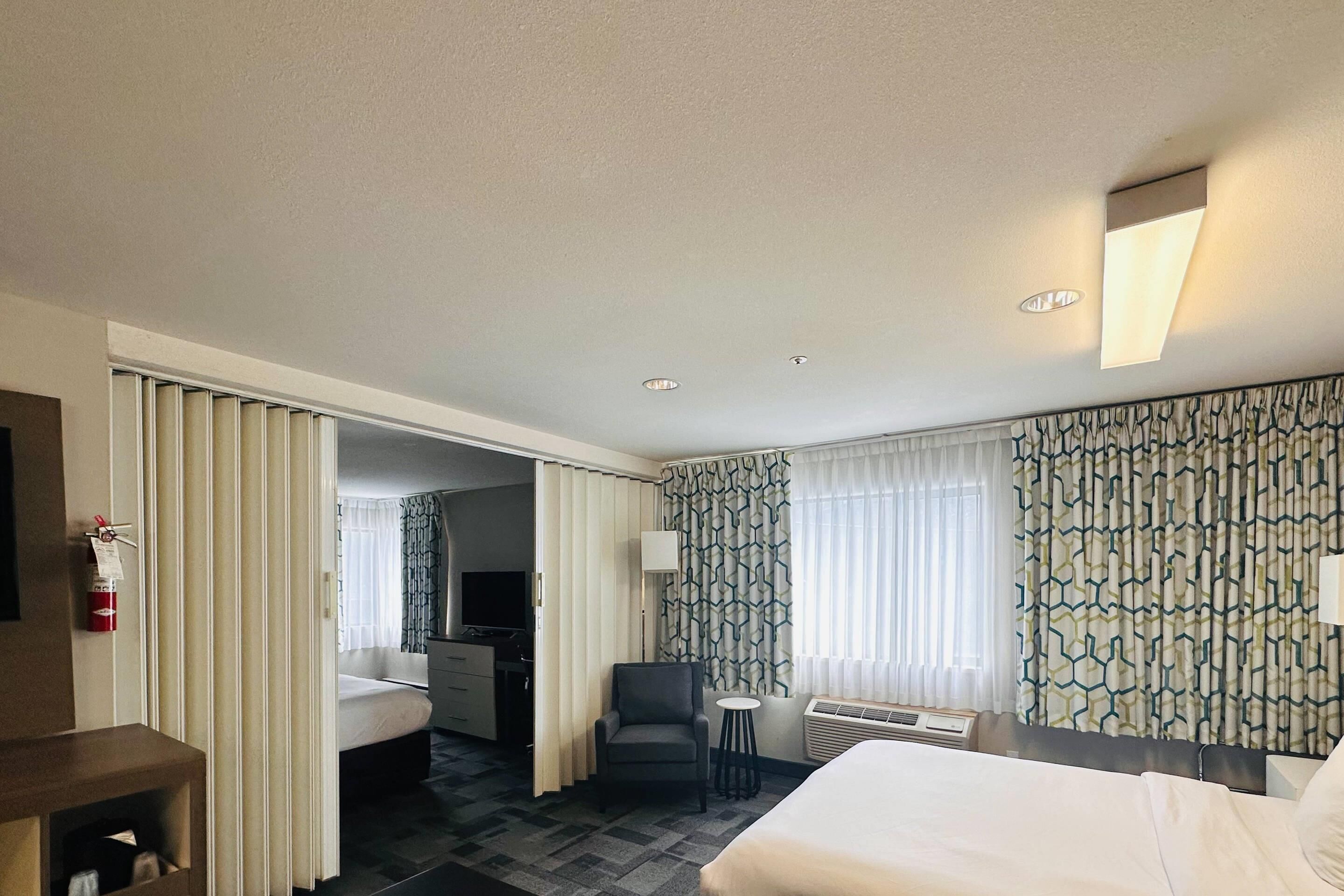 A hotel room with a bed, a desk, a chair, a small table, and a TV.