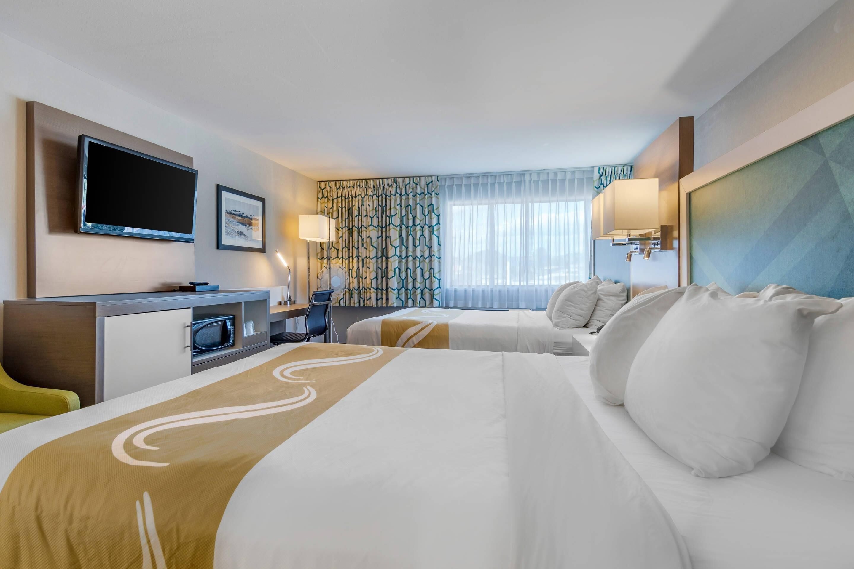 A hotel room with a bed, a desk, a television, and a window with curtains.