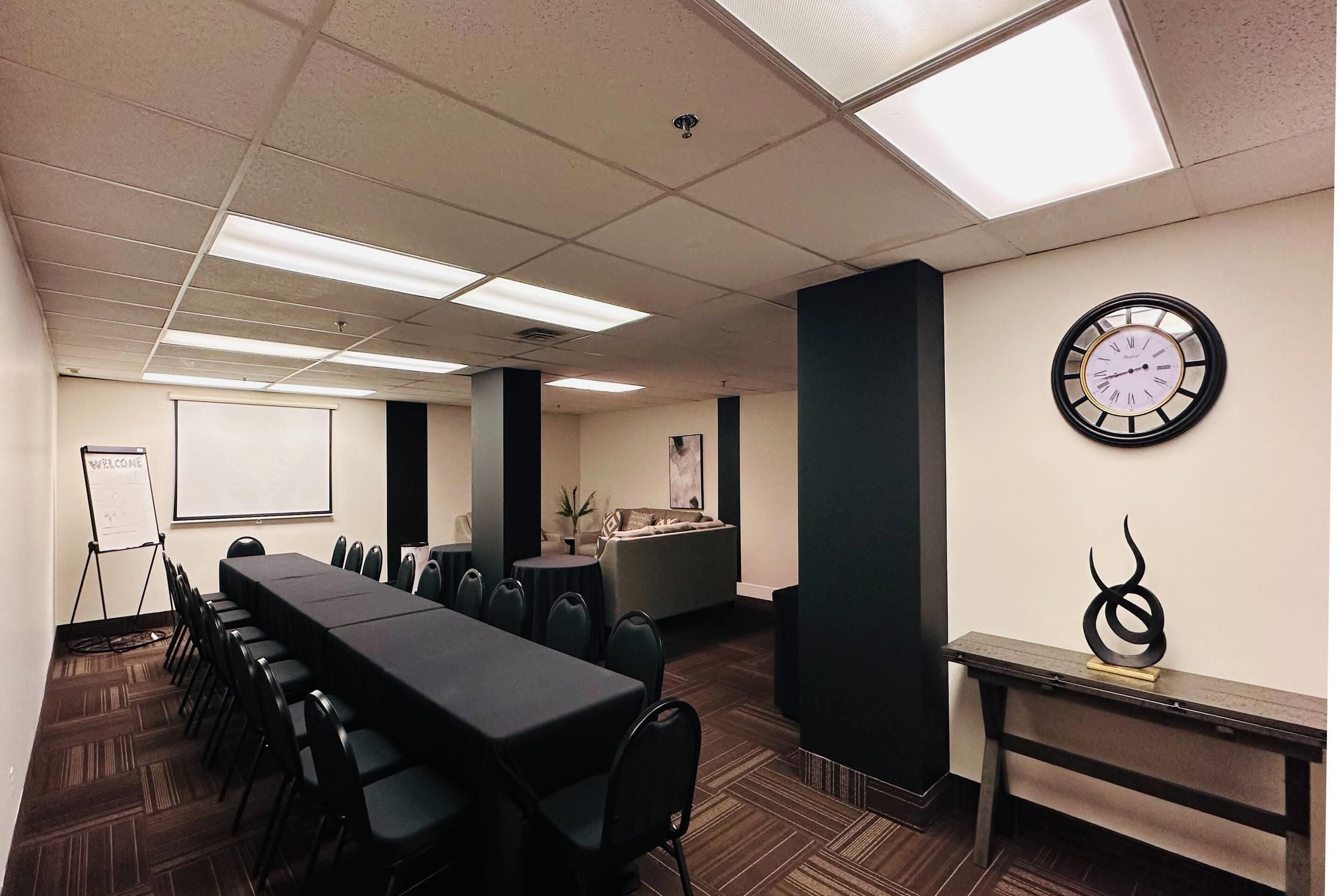 Une salle de conférence avec une longue table, des chaises, une horloge et un tableau blanc.