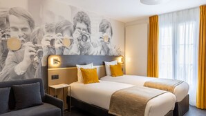 Ein Hotelzimmer mit zwei Betten, einem Sofa, einer Wand mit einem großen Foto und einem Fenster mit gelben Vorhängen.