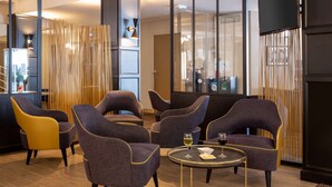 Ein moderner Lounge-Bereich mit verschiedenen Sitzgelegenheiten, darunter Stühle und Sofas, angeordnet um einen zentralen Tisch mit Glasplatte.