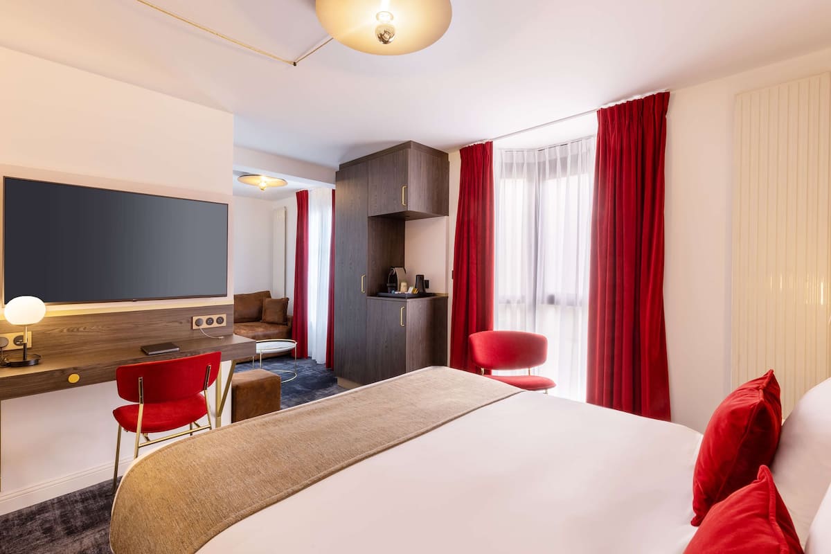 A hotel room with a large bed, a desk with a computer, a chair, a TV, and a wardrobe.