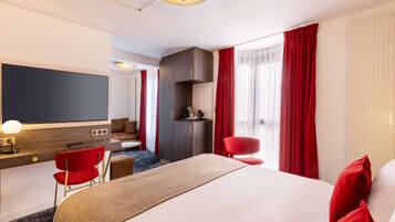 A hotel room with a large bed, a desk with a computer, a chair, a TV, and a wardrobe.