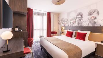 Een hotelkamer met een groot bed, een bureau met lamp, een stoel, een kledingkast en een muur met een fotoprint.