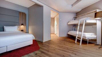 Una habitación de hotel moderna con una cama grande, un tapete rojo, una cama litera y suelo de madera.