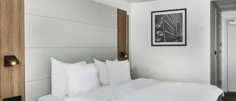 Una habitación de hotel moderna con una cama, mesitas de noche, una lámpara de pared y un cuadro enmarcado.