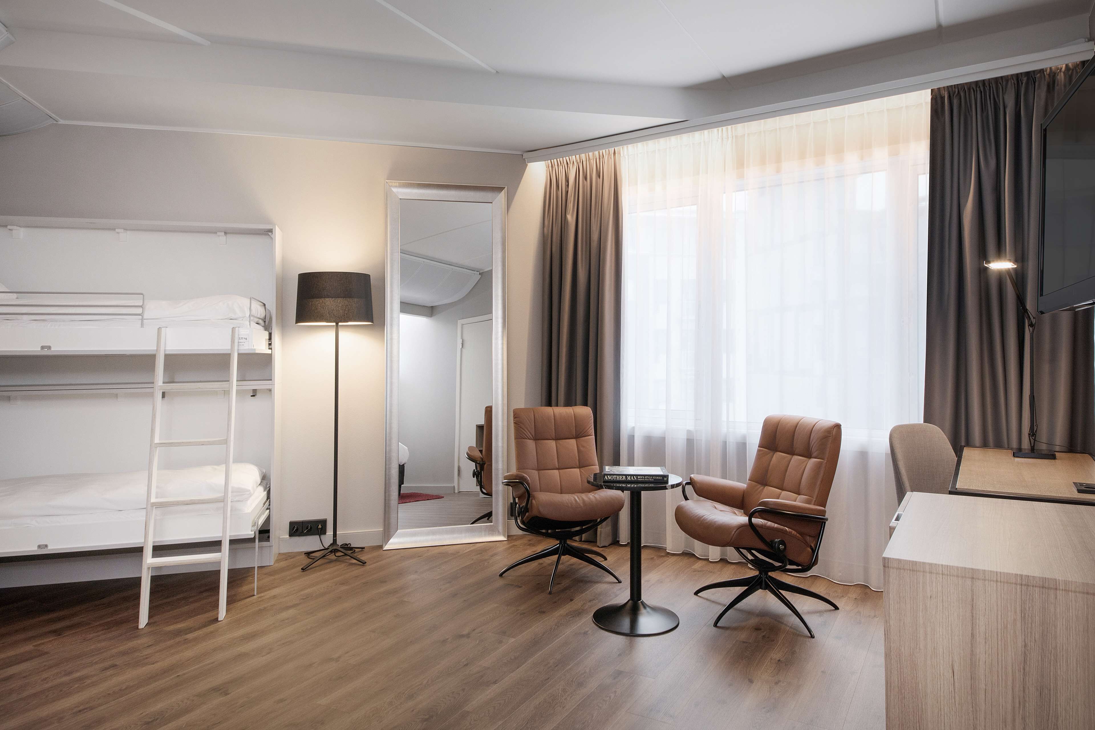 Ett hotellrum med en våningssäng, två läderfåtöljer, ett litet bord och ett skrivbord.