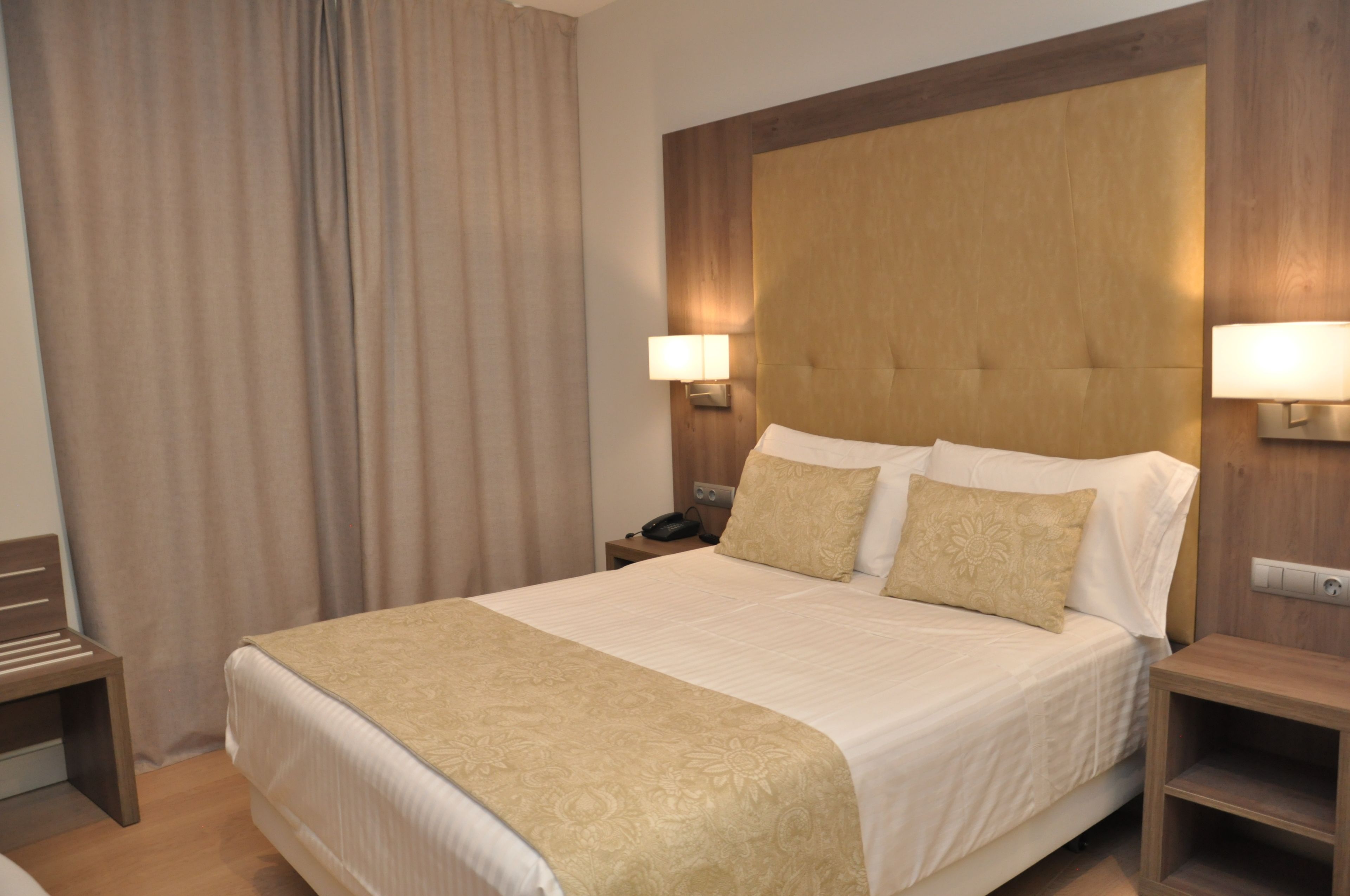 A hotel room with a large bed, two bedside lamps, a wooden headboard, and a nightstand with a phone.