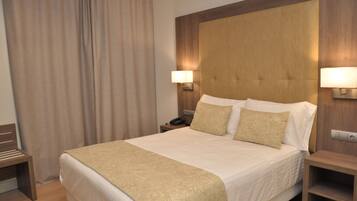 A hotel room with a large bed, two bedside lamps, a wooden headboard, and a nightstand with a phone.