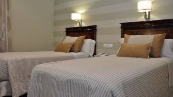 A hotel room with two beds, striped bedding, a wooden headboard, a nightstand, and a wall-mounted lamp.