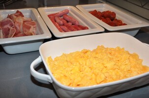 Tres fuentes blancas rectangulares con distintos alimentos: una con jamón, otra con salchichas y otra con salsa roja.