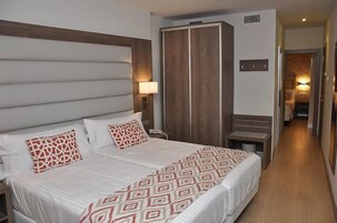 Una habitación de hotel con una cama grande, un armario, una mesita de noche y una lámpara.