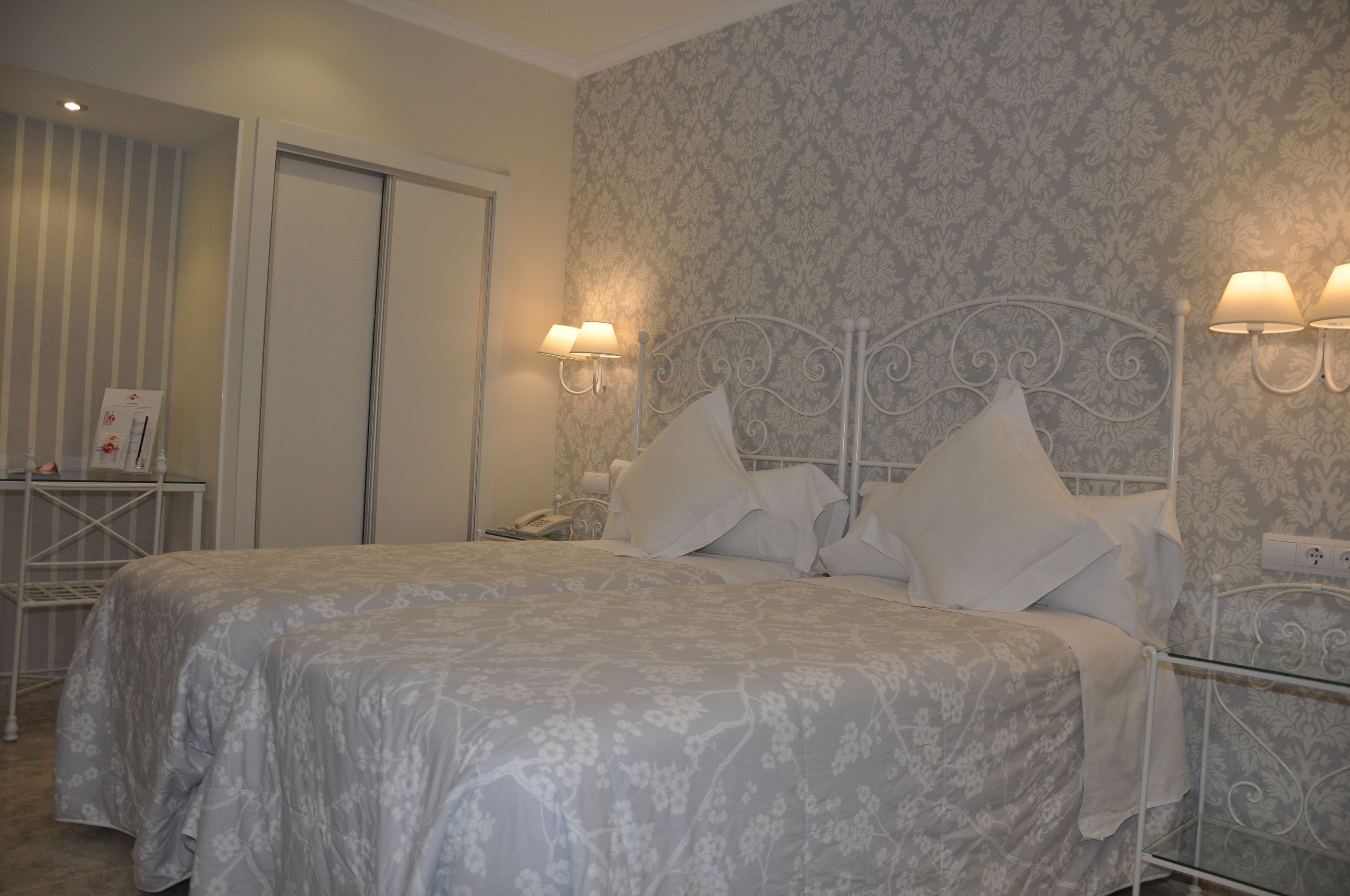 Una cama doble con cubrecama floral, dos lámparas de pared y un papel tapiz estampado.