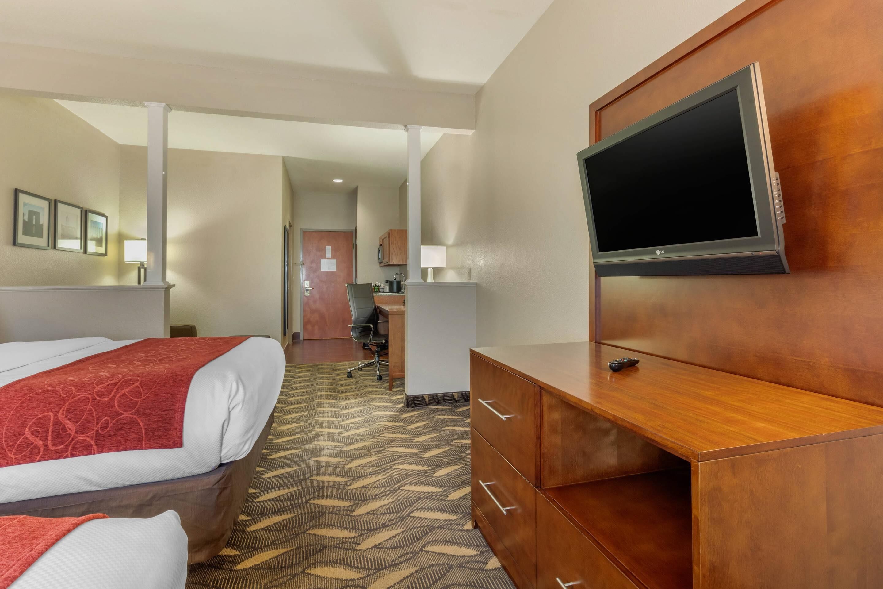 A hotel room with a bed, a wooden dresser, a television, and a desk with a chair.