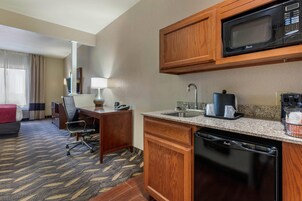 Una habitación de hotel con kitchenette, un escritorio con silla, una cama y un baño.