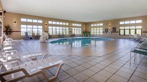 Una amplia piscina cubierta con varias pistas, rodeada de habitaciones iluminadas por el sol con ventanas grandes y varias sillas de descanso.