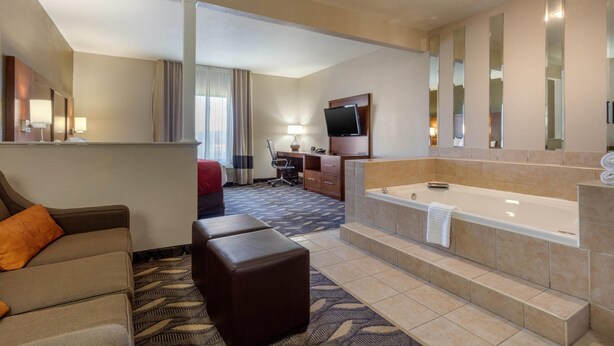 Habitación de hotel con sofá, reposapiés, una bañera grande, escritorio con silla, televisor y espejo.