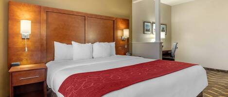 A hotel room with a large bed, a wooden headboard, two bedside tables with lamps, and a red throw blanket.