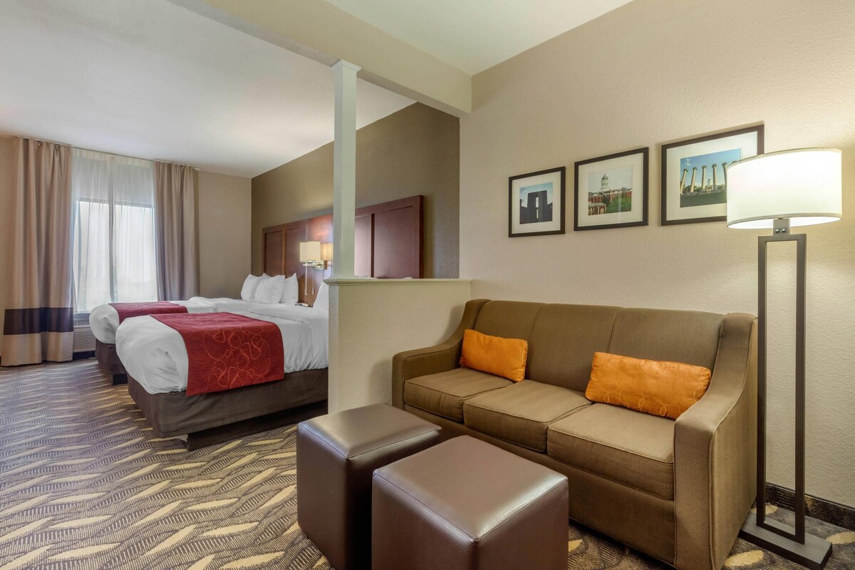 A hotel room with a bed, two sofas, a coffee table, and a lamp.