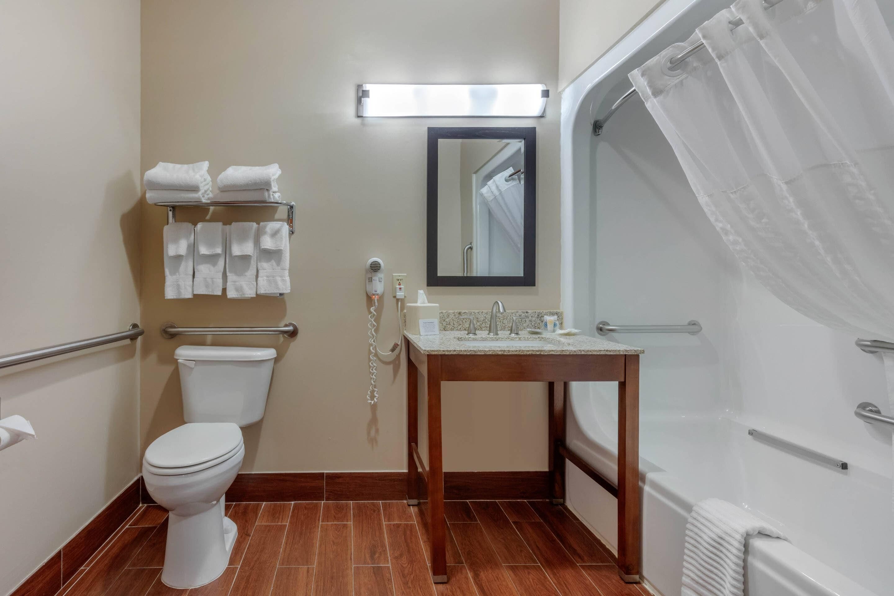 A bathroom with a toilet, sink, and shower. There are towels on a rack and a mirror above the sink.