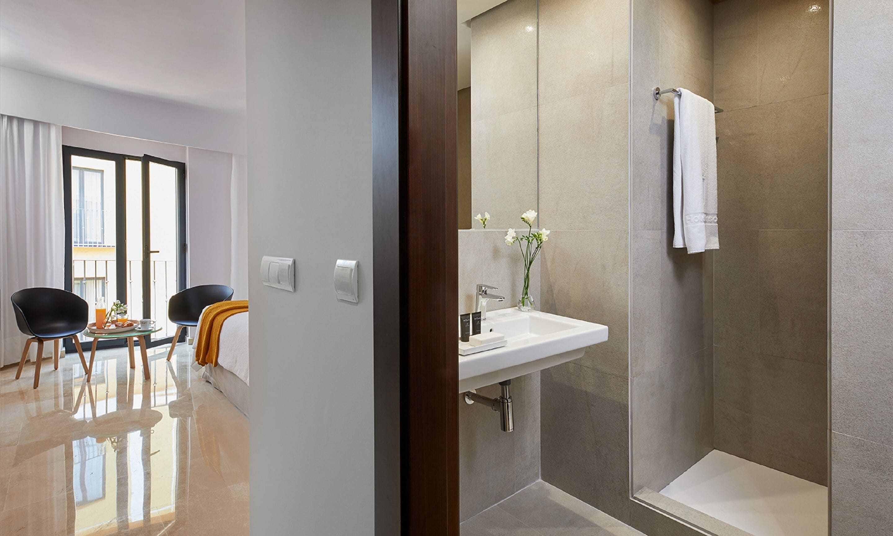 Una habitación de hotel moderna con zona de comedor, baño con ducha y un gran ventanal.