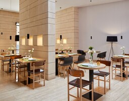 Un comedor moderno con mesas y sillas de madera, dispuesto en un espacio amplio.