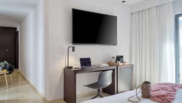 Una habitación de hotel moderna con una cama, un escritorio con silla, un televisor de pantalla plana y un ventanal con cortinas.